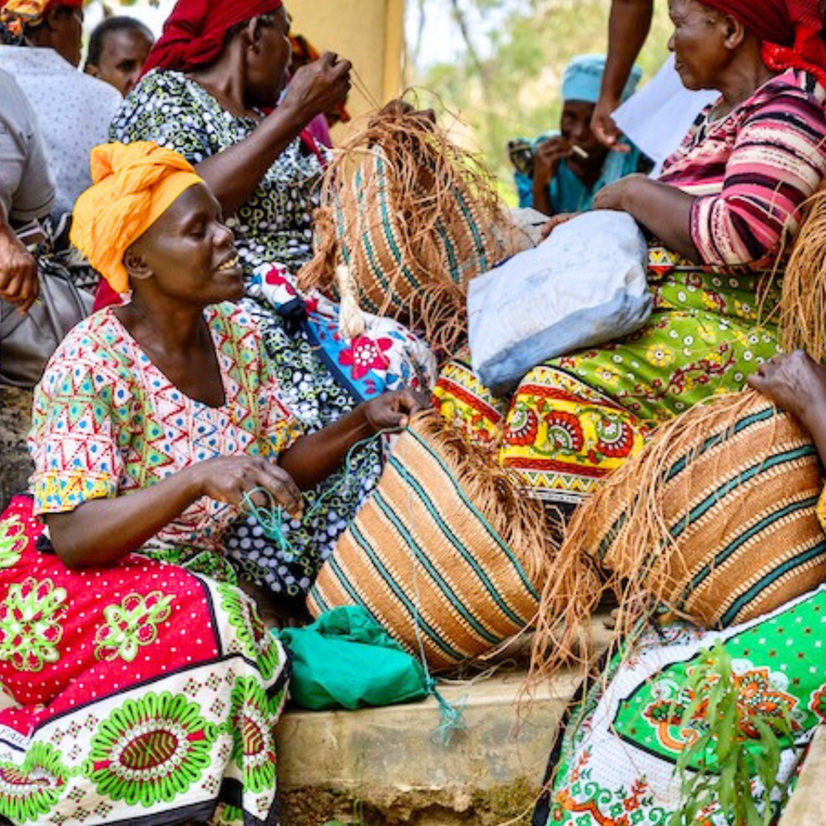 Group of women sitting together, wearing colorful traditional clothing in a communal setting.